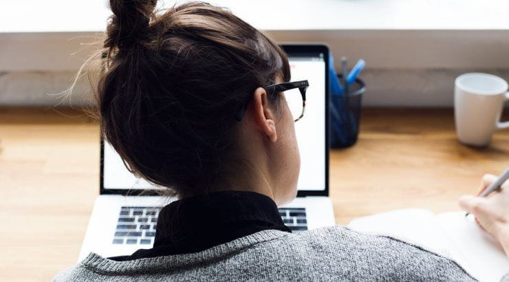 female taking notes and browsing on laptop