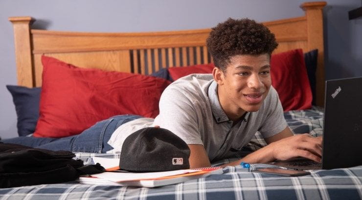 boy on bed writing on laptop