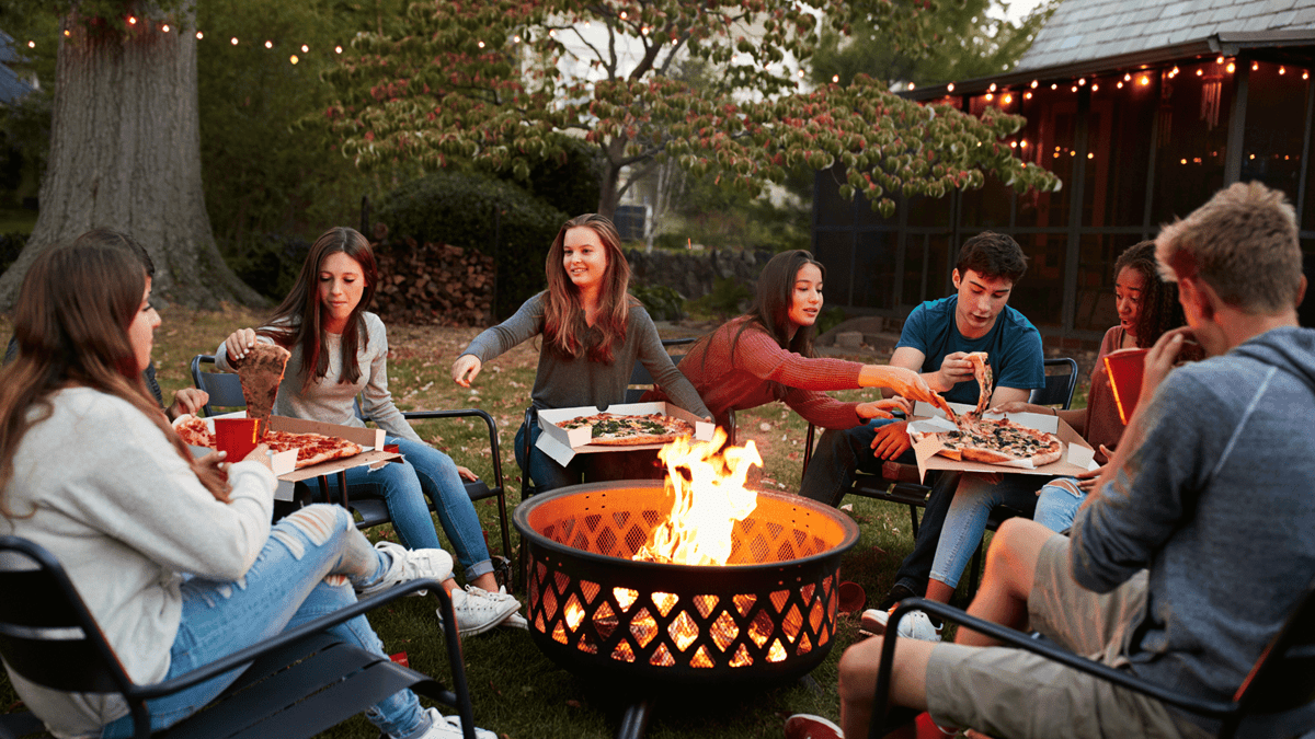 college students eating pizza around fire