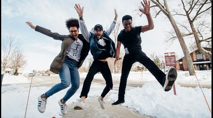 three college students jumping for joy outside in the snow