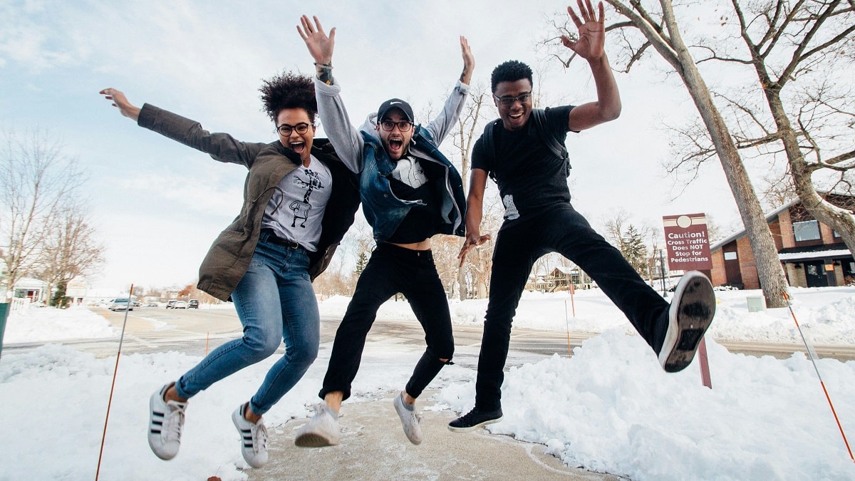 three college students jumping for joy outside in the snow