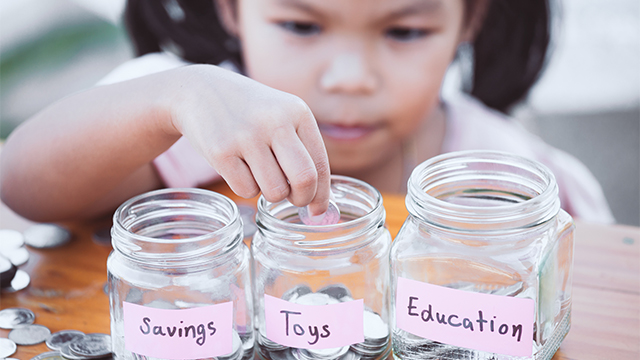 Young child saves money in jars marked for separate goals.
