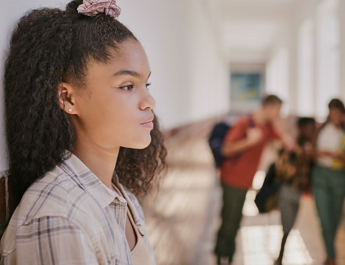 Young sad teenage girl feeling lonely and excluded at school. Female outside classroom and thinking about teen problems, bullying or trouble feeling depressed and anxiety.
